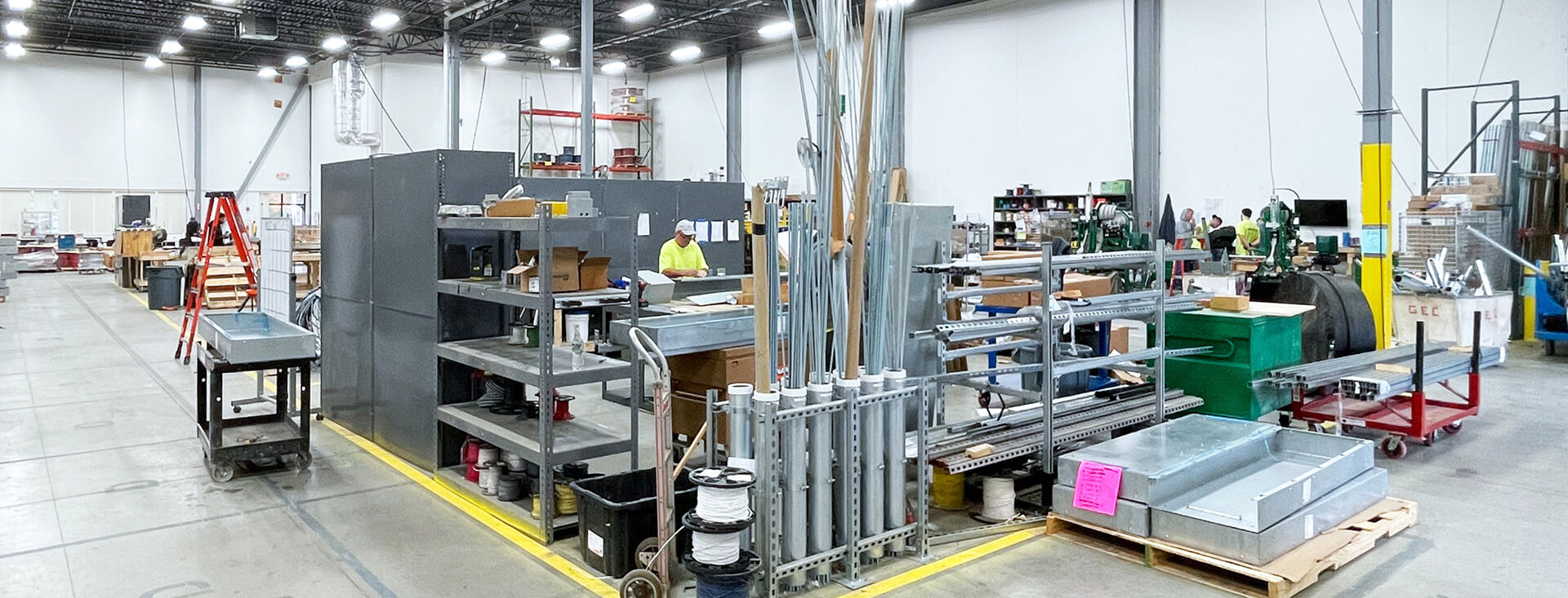 Photo of inside a warehouse with industrial equipment, and three people wearing yellow shirts.