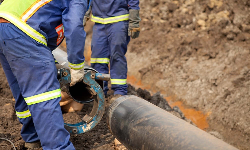 Two people working on pipes in a trench.