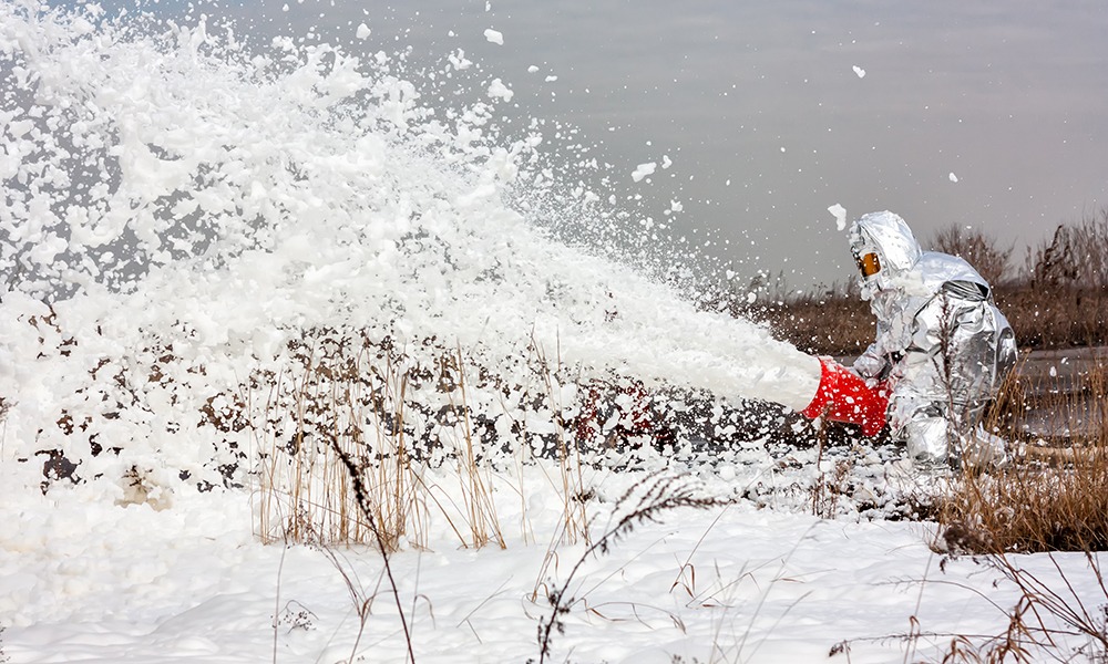 A person sprays aqueous film-forming foam (AFFF) on the ground.