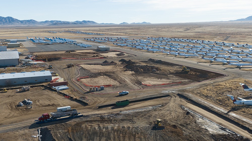 Excavation pit in foreground with dozens of airplanes parked in background at Kingman Municipal Airport.