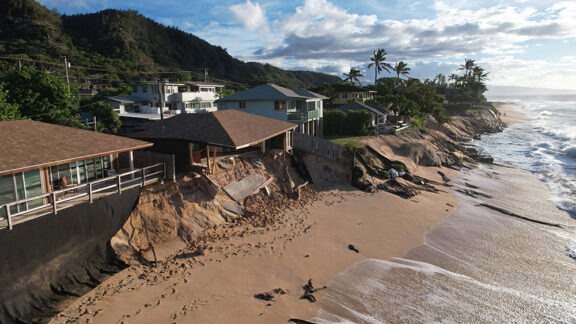 Homes along a sandy coast show severe erosion after ocean waves damaged the shoreline.