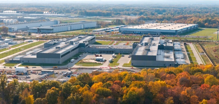 Aerial view of a large campus with multiple low-rise buildings surrounded by autumn-colored trees.