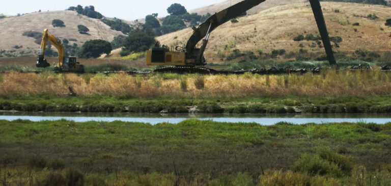 Two excavators construct a deep-soil bentonite cutoff for seepage through a levee.