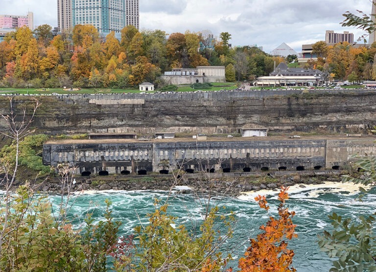 Autumn foliage surrounds a river, as aging power structure, and a city skyline